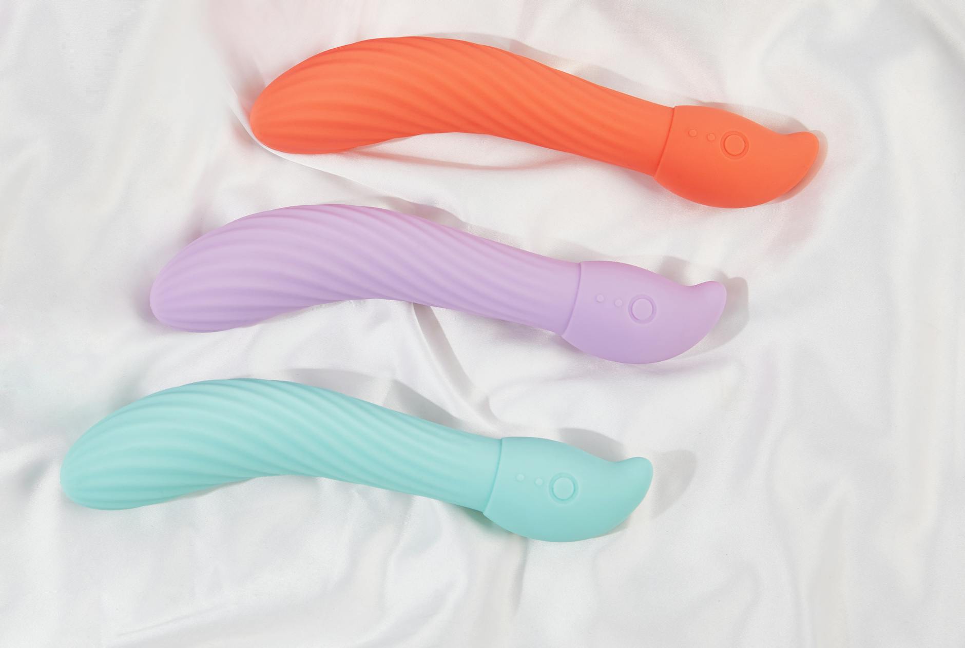 Eine Hand hält einen modernen orangefarbenen Vibrator vor minimalistische lila Kulisse