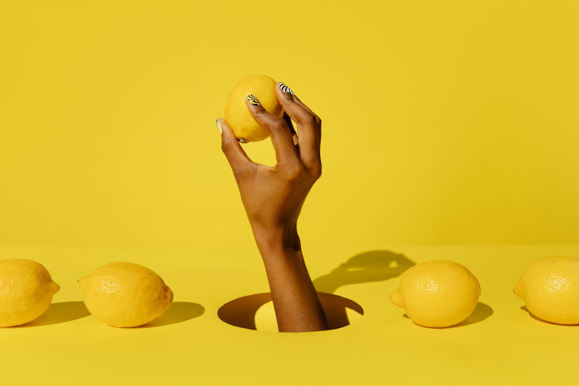 Eine Hand hält eine frische Zitrone vor gelbem Hintergrund, symbolisch für die erfrischende Stimulation des Lemon-Vibrators