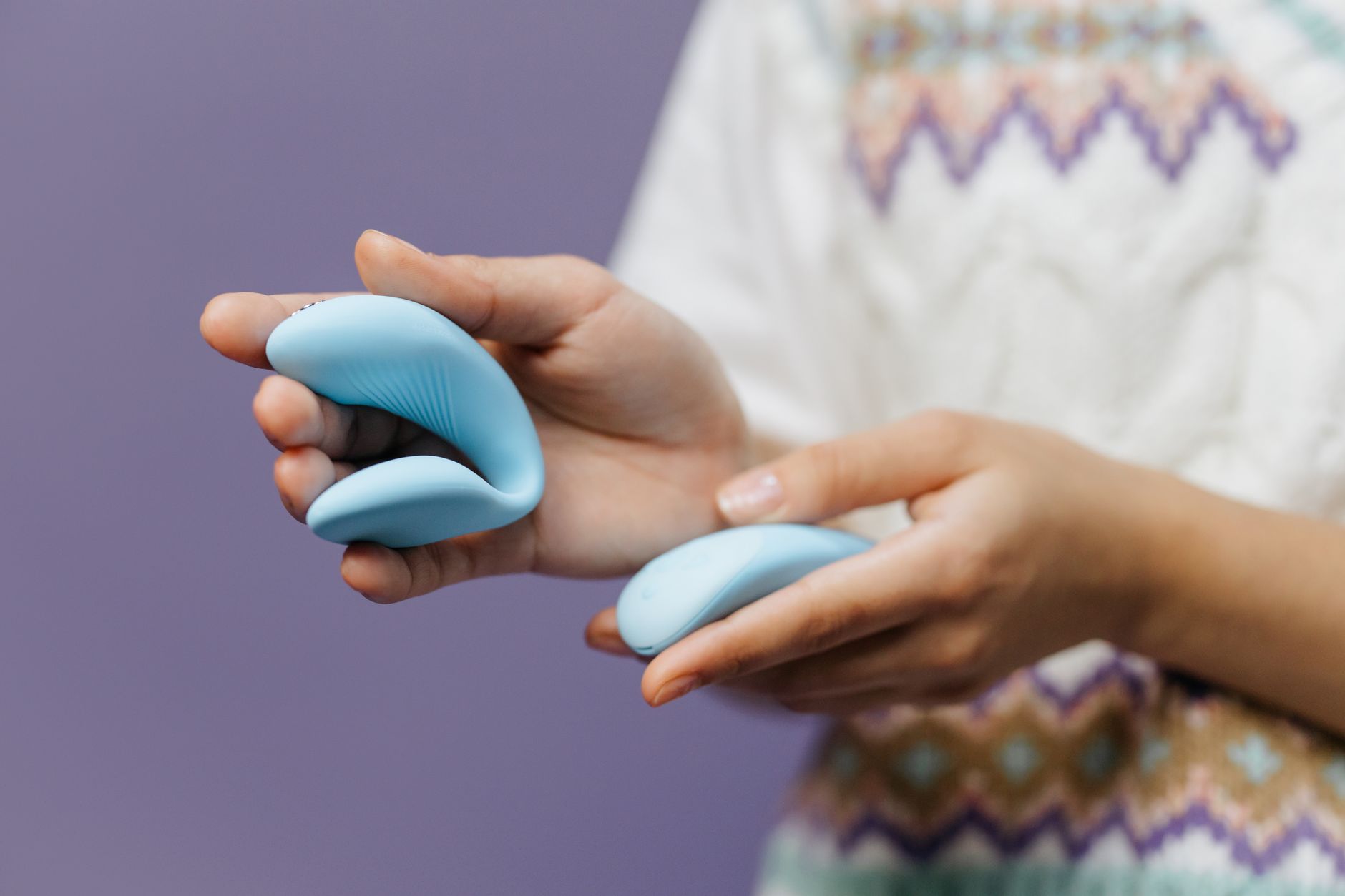 Close-up of hands holding a blue vibrator against a purple background