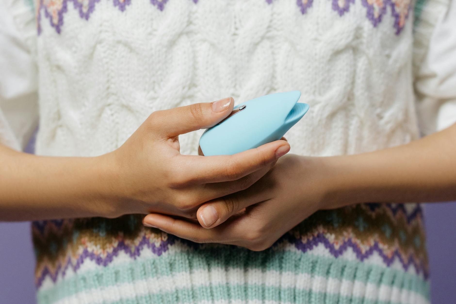 Eine Hand hält einen blauen Lem-Vibrator gegen einen gestrickten Pullover, Symbol für alltägliche Lust und Selbstfürsorge