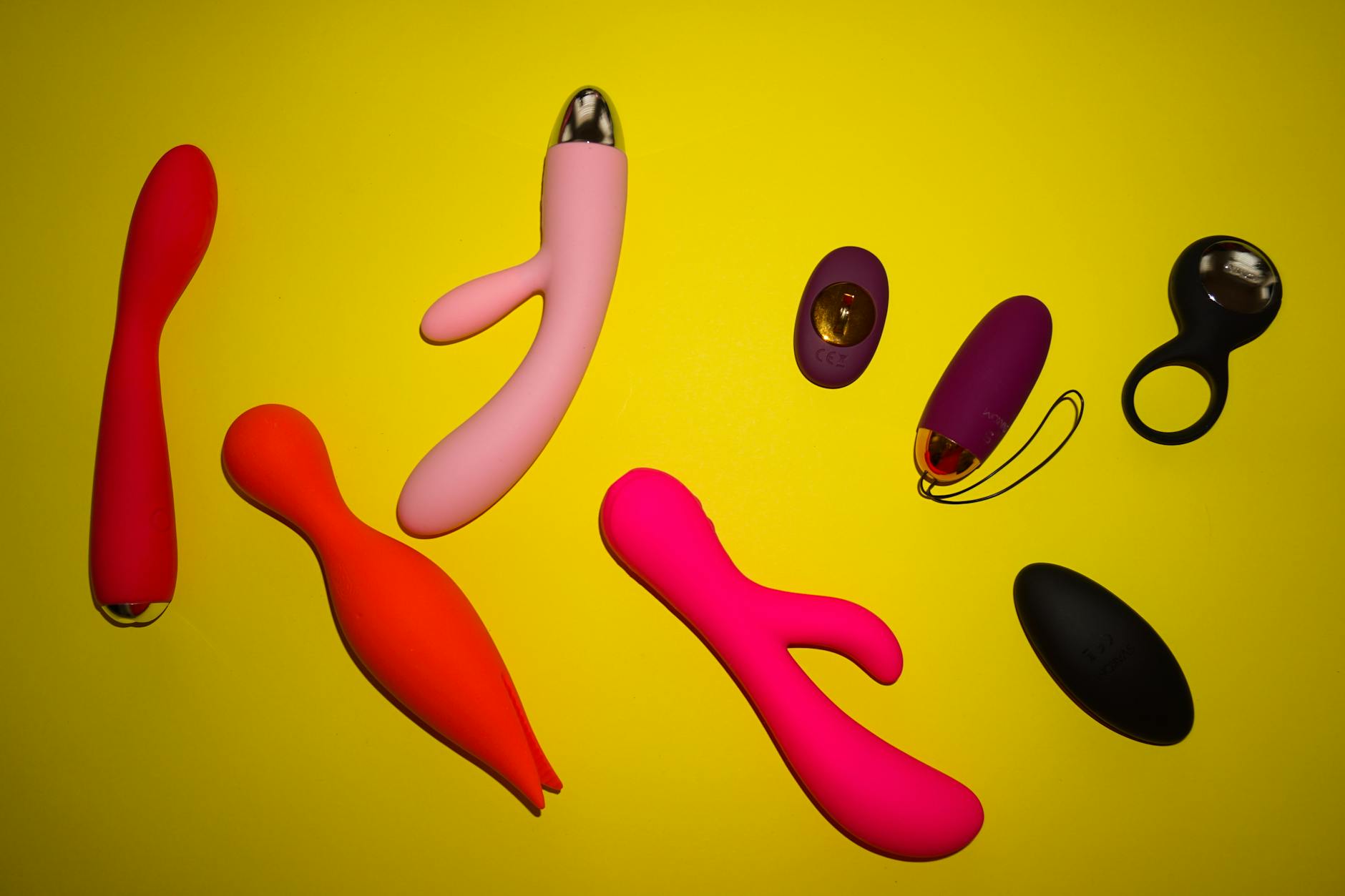 Farbenfrohe Ansammlung verschiedener Sexspielzeuge auf leuchtendem gelben Hintergrund, darunter Lemon-Vibratoren und andere Designs