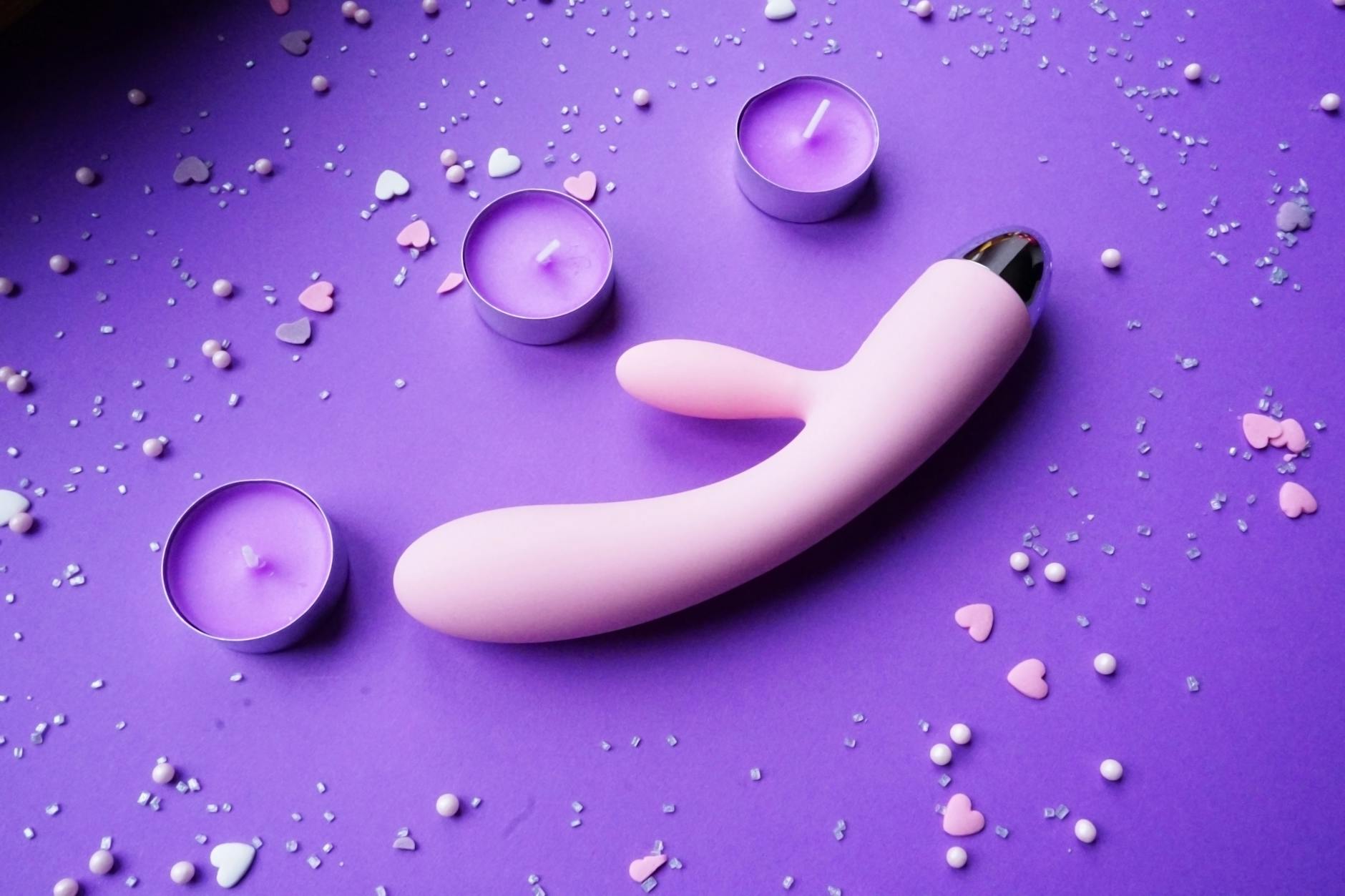 Rosa Lemon-Vibrator auf lila Hintergrund mit Herzgeflüster und Kerzen für romantische Atmosphäre