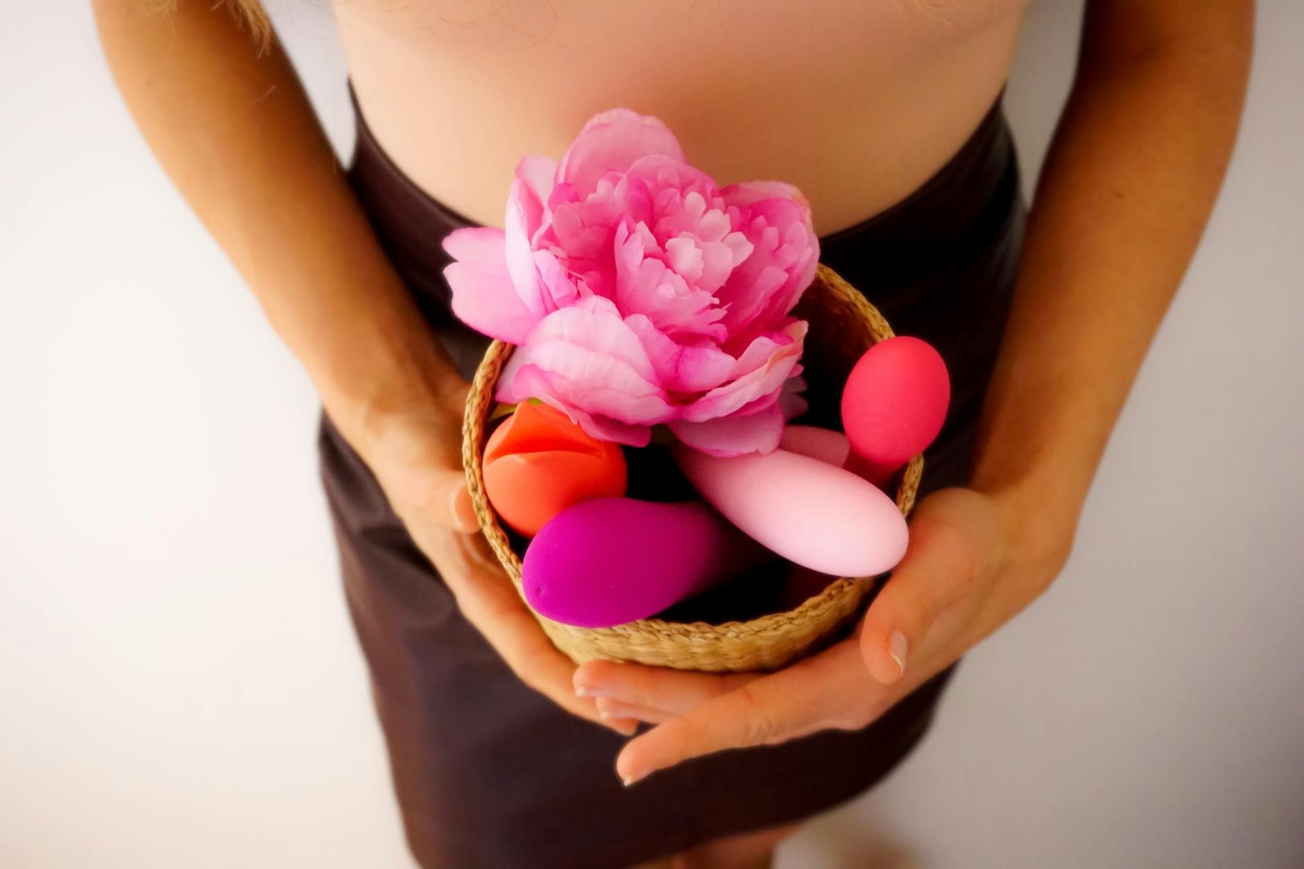 Zwei Hände halten rosa und blaue Silikonvibratoren vor pastellfarbenem Hintergrund
